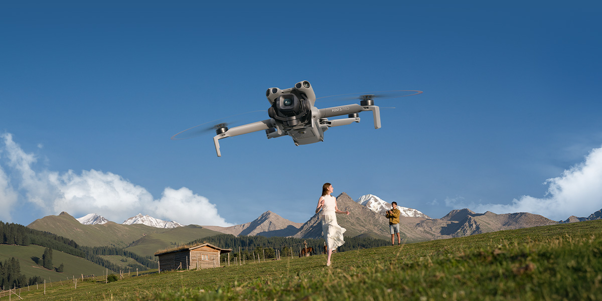 Dron w locie nad łąką w górach, za nim mężczyzna i kobieta