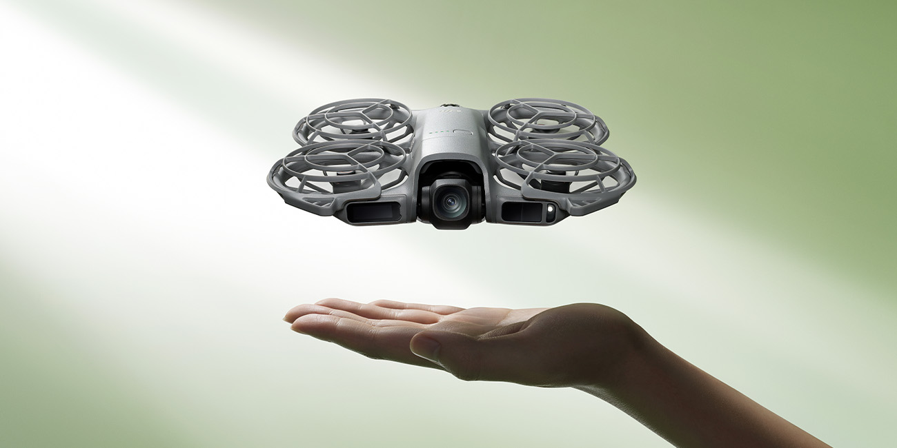 Dron DJI Neo 2 unoszący się nad dłonią na zielonym tle