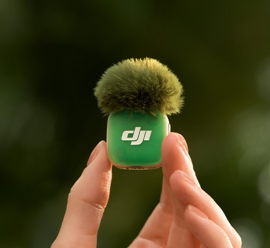 Zielony nadajnik DJI Mic Mini 2 z osłoną przeciwwietrzną trzymany w palcach