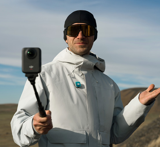 Turysta w jasnej kurtce nagrywa vloga za pomocą kamery sportowej na wysięgniku