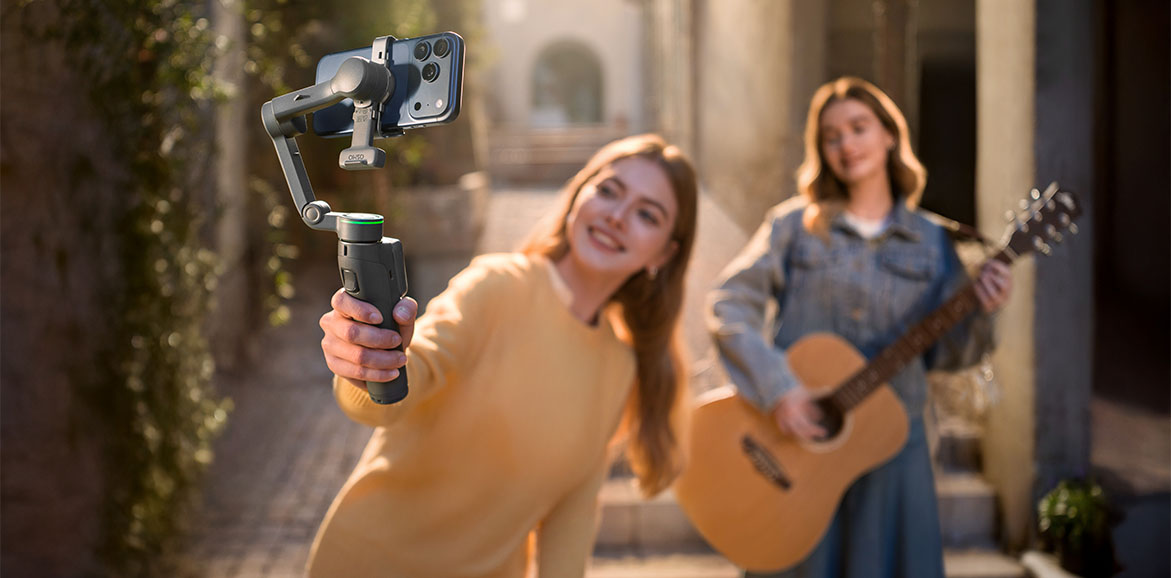 Dwie dziewczyny – jedna gra na gitarze, a druga nagrywa wideo smartfonem na gimbalu
