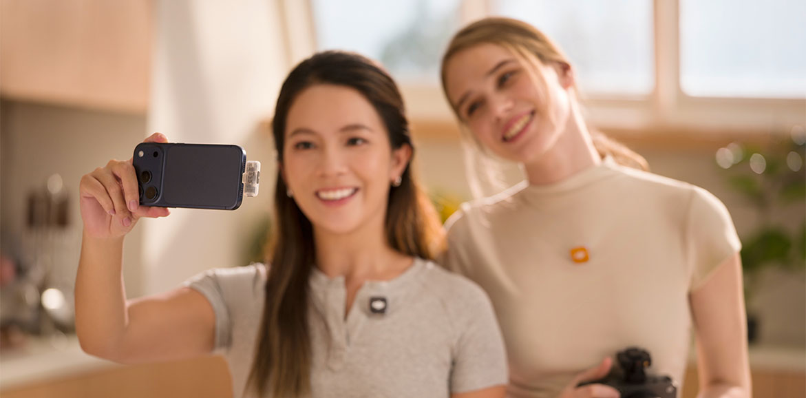 Uśmiechnięte kobiety z przypiętymi mikrofonami DJI Mic Mini 2S nagrywają wideo smartfonem