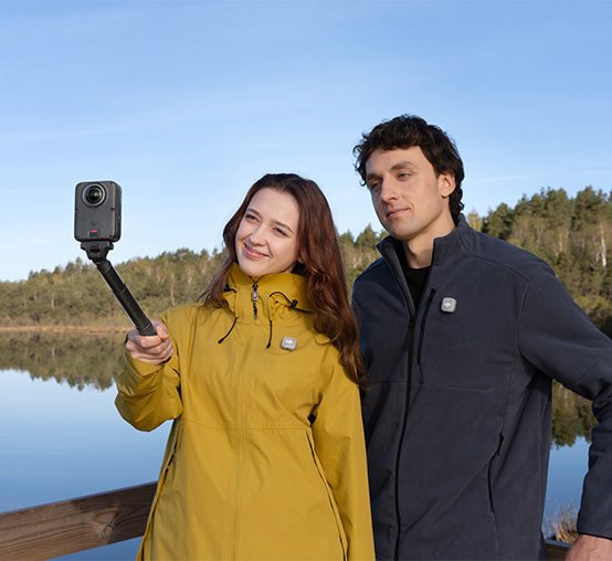 Kobieta i mężczyzna robią sobie zdjęcie na tle jeziora kamerą DJI Osmo 360 II