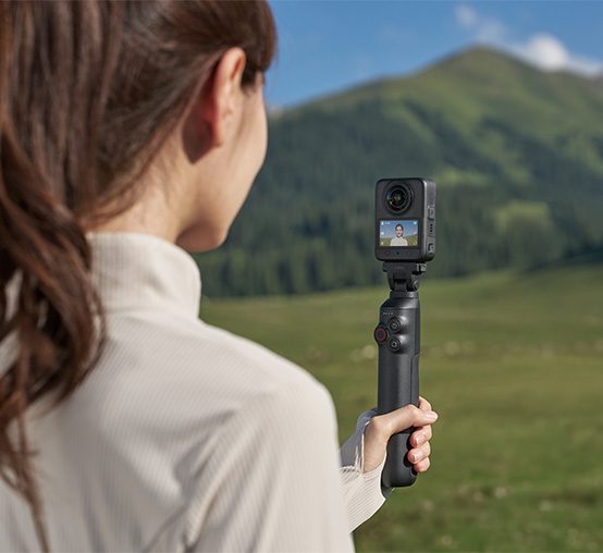 Kobieta trzyma nagrywającą kamerę DJI Osmo 360 II na Battery Extension Rod